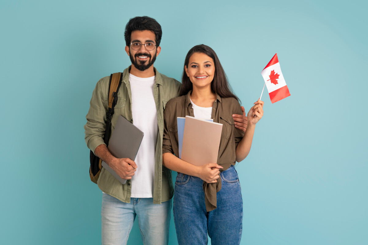 Education abroad, immigration to EU, language school. Cheerful multicultural young arab man and indian woman students with Canadian flag, books and laptop on blue background
